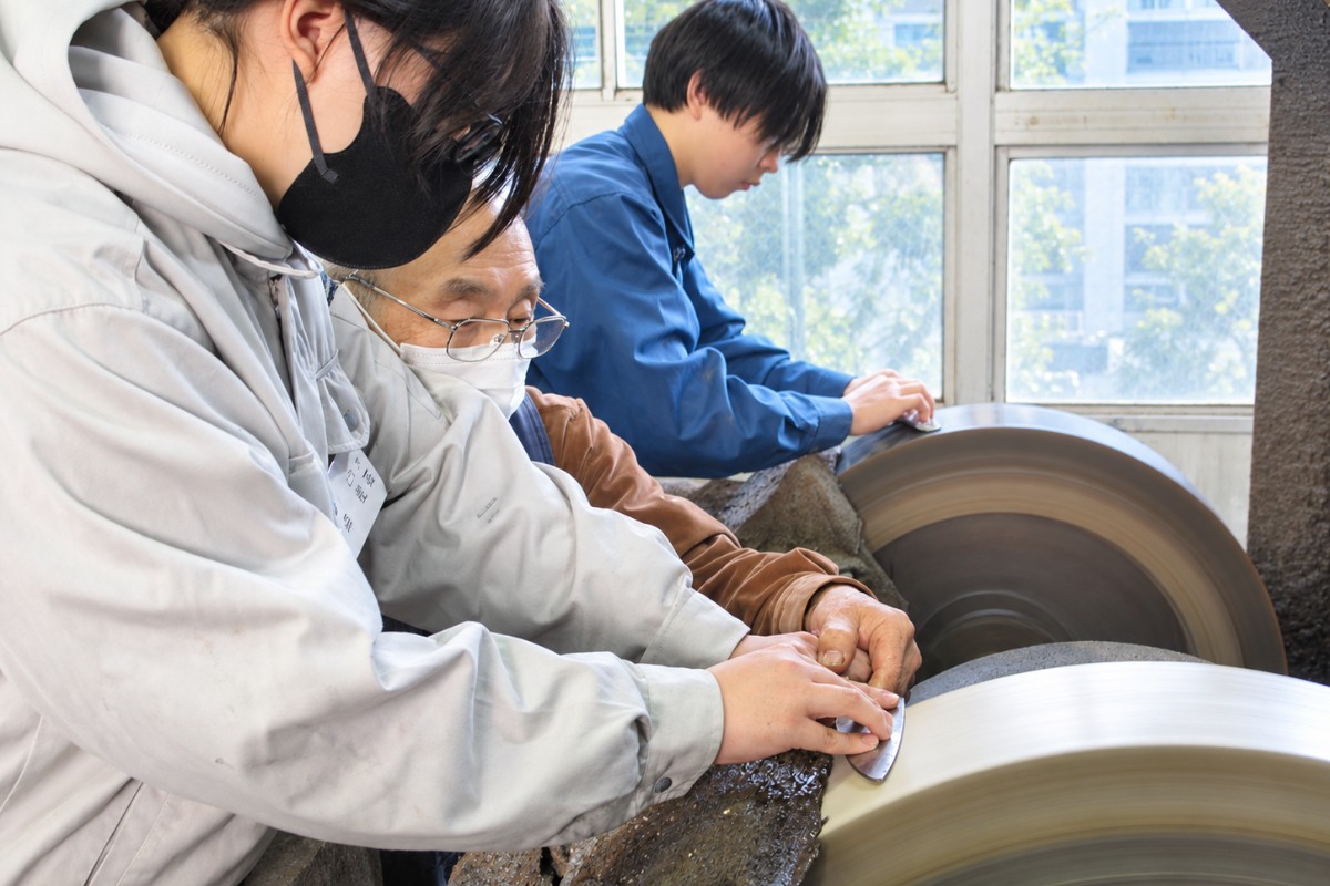 職人の指導を受けながら刃物の研ぎ作業に取り組む生徒